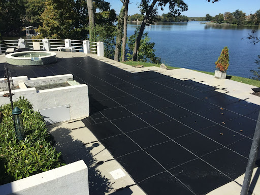 An in-ground pool with a LOOP-LOC black mesh cover is shown next to a lake.
