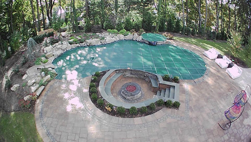 An in-ground pool with a green LOOP-LOC cover is shown from above in a wooded area.