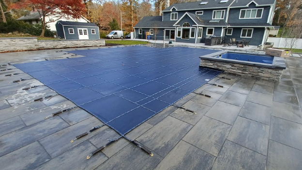 A LOOP-LOC pool cover is installed on an outdoor pool in front of a large, gray house.